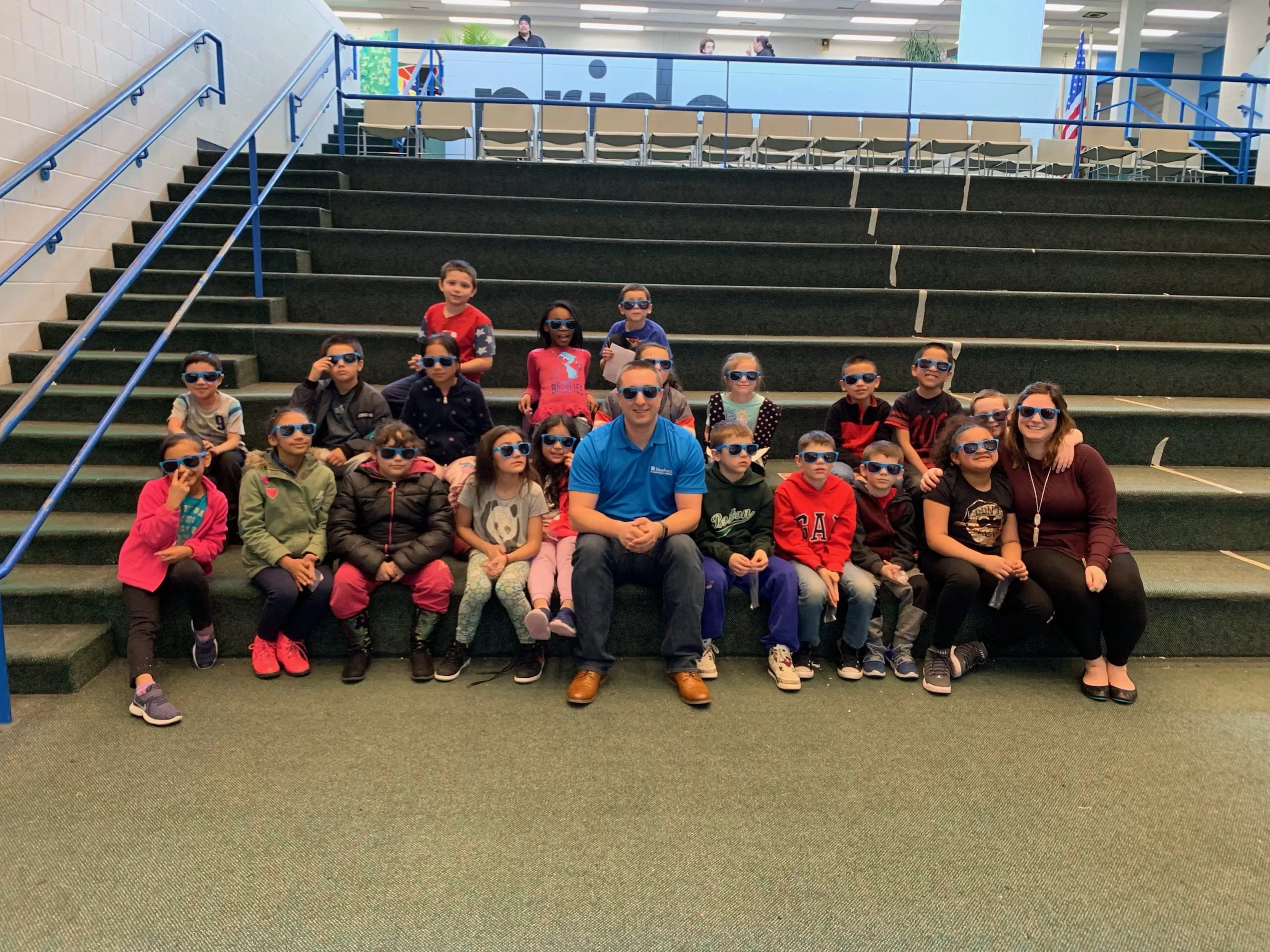 A group of kids, a teacher, and Jonathan sitting on steps all wearing Bluehost sunglasses.