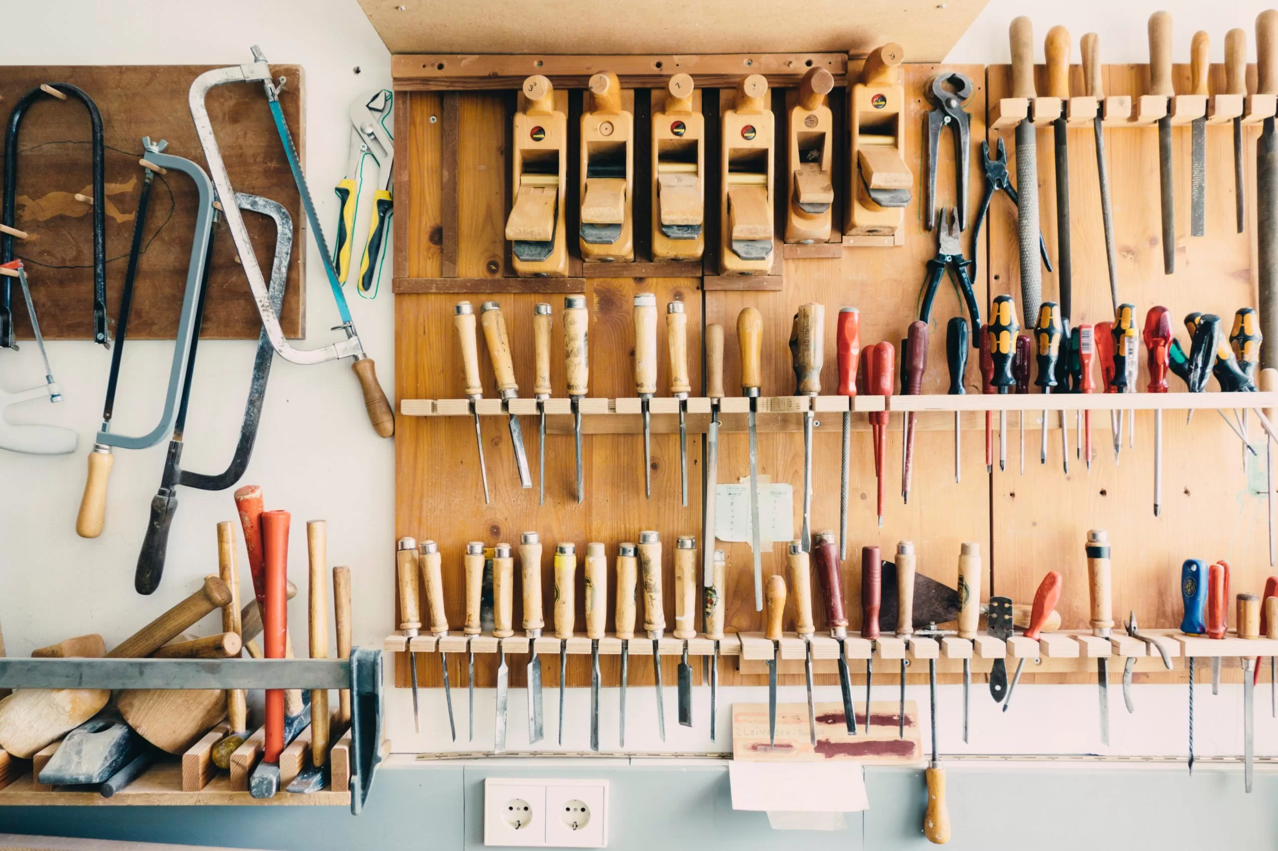 A workbench in front of a tool rack on the wall with saws and chisels