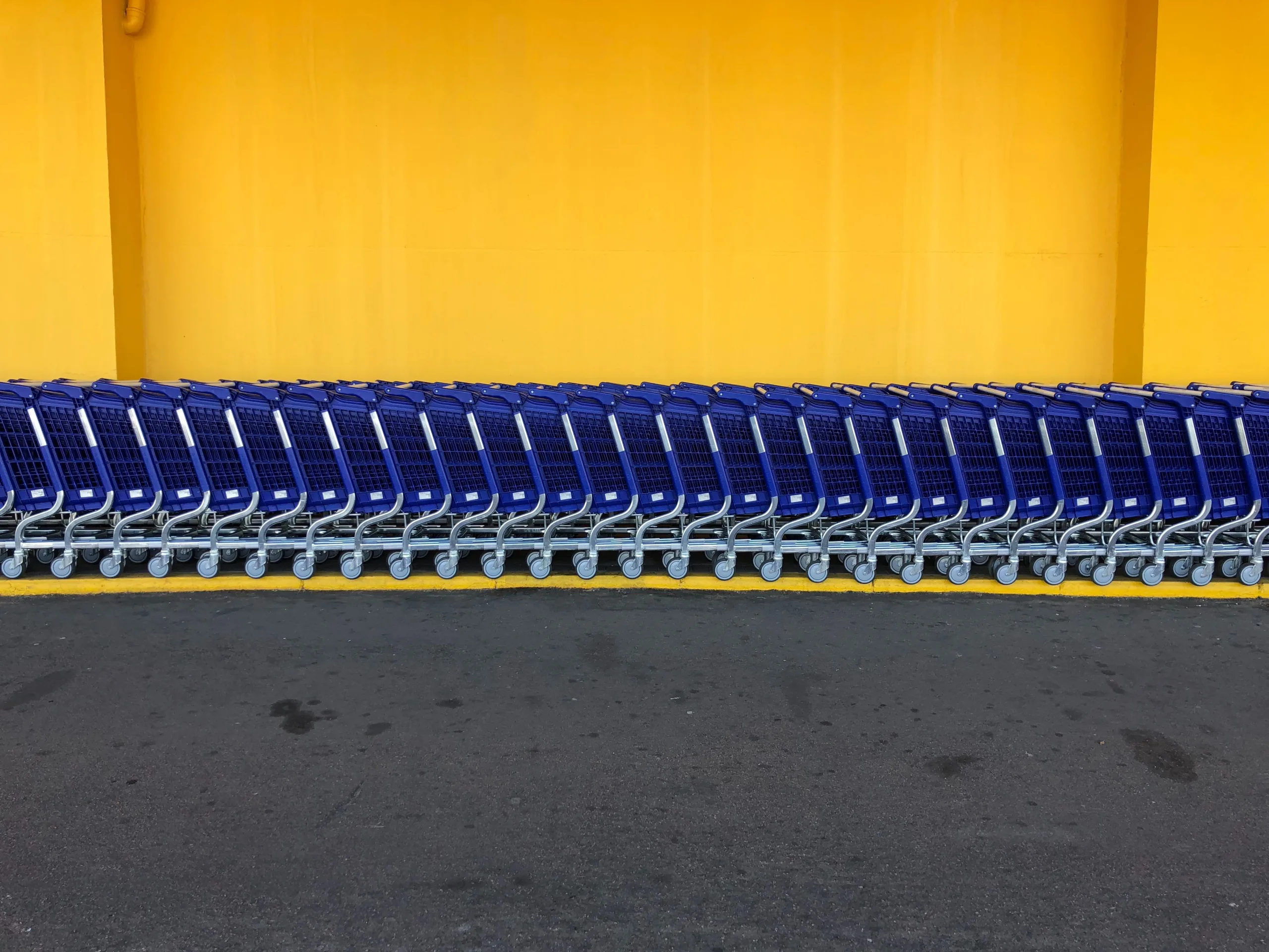 A row of blue shopping carts lined against a bright yellow wall.