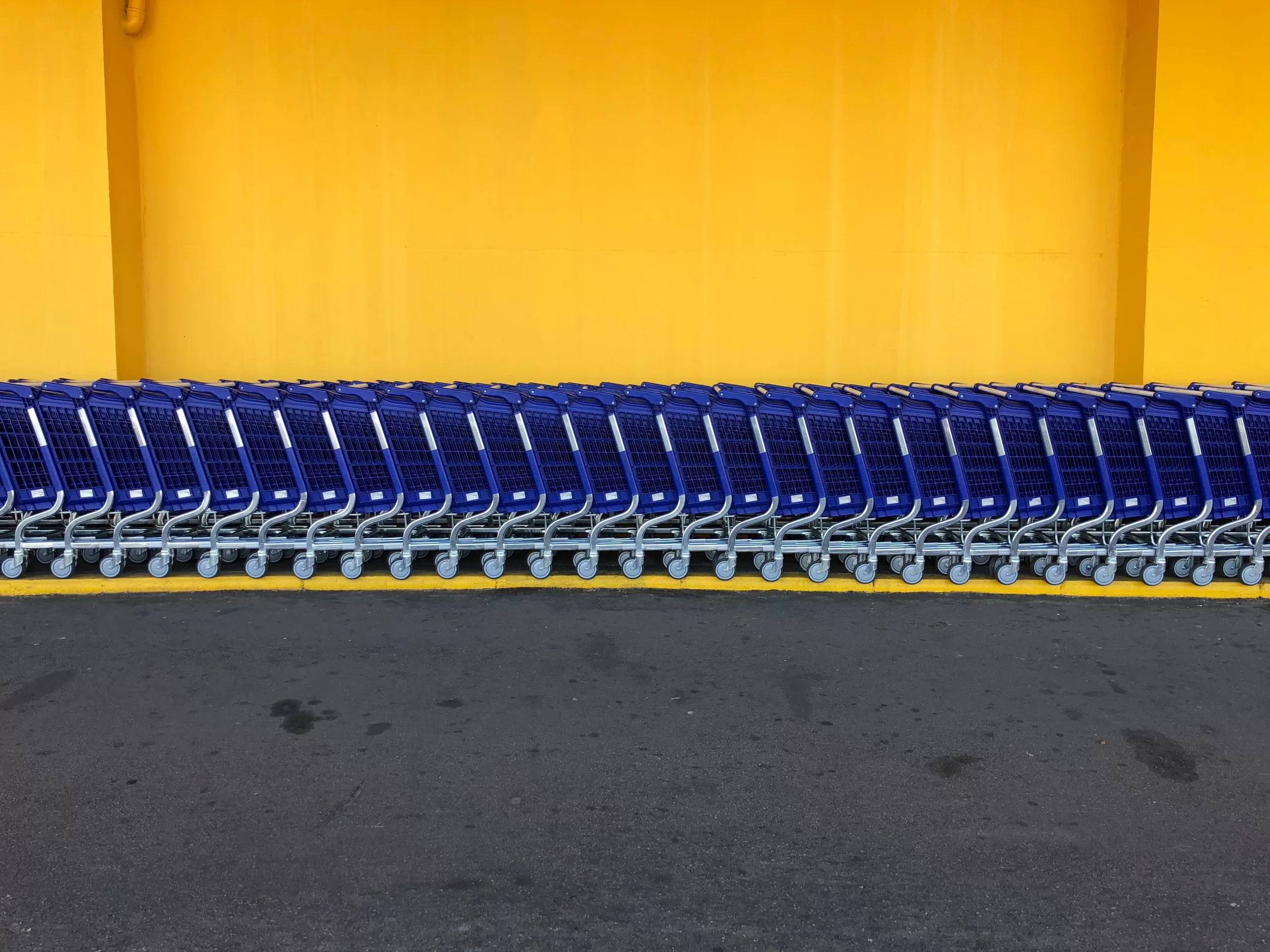 A row of blue shopping carts lined against a bright yellow wall.