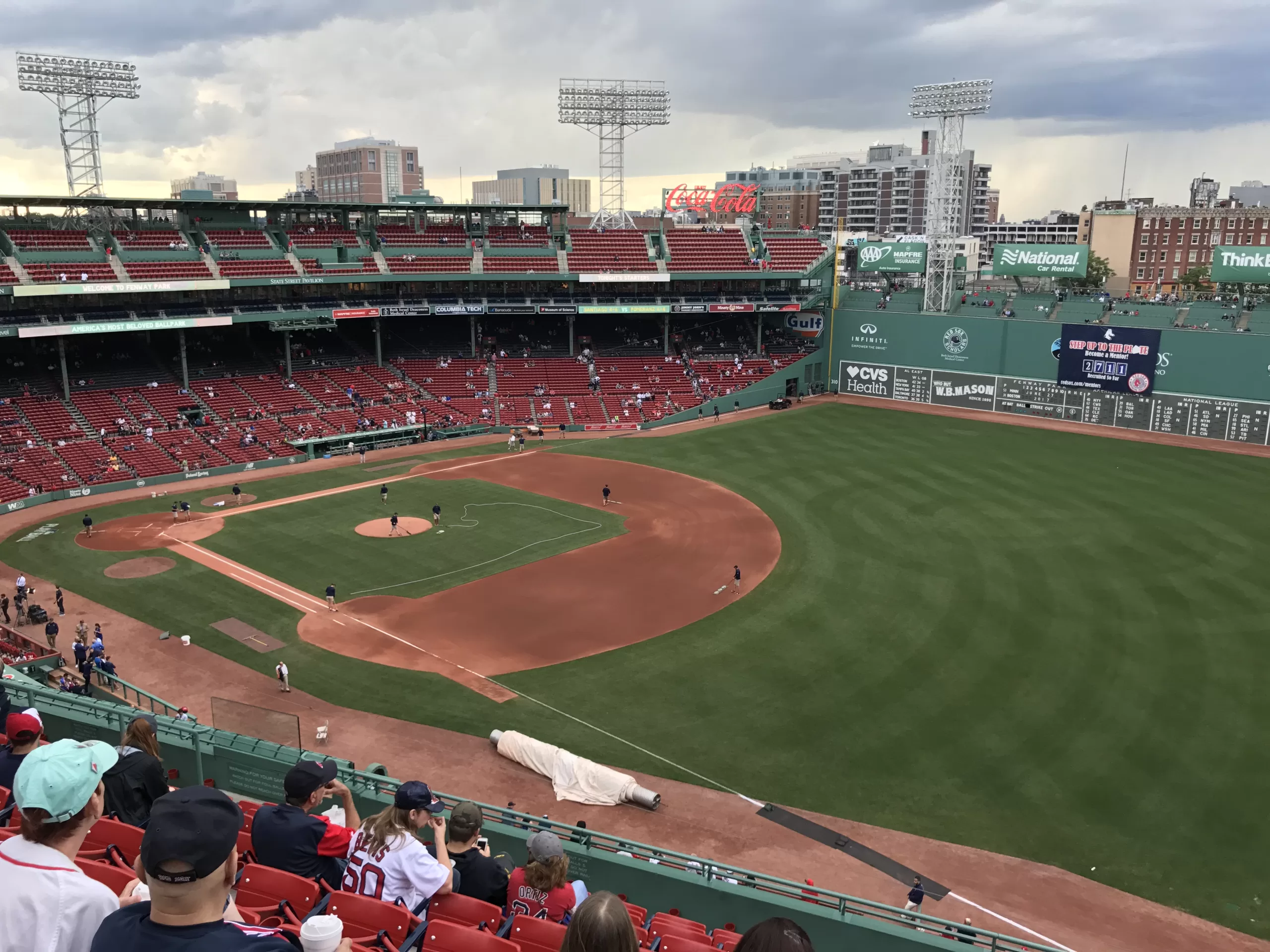 A pre-game view of Fenway Park from the upper level down the right field foul line. The grounds crew is preparing the field, and the Green Monster is in view.
