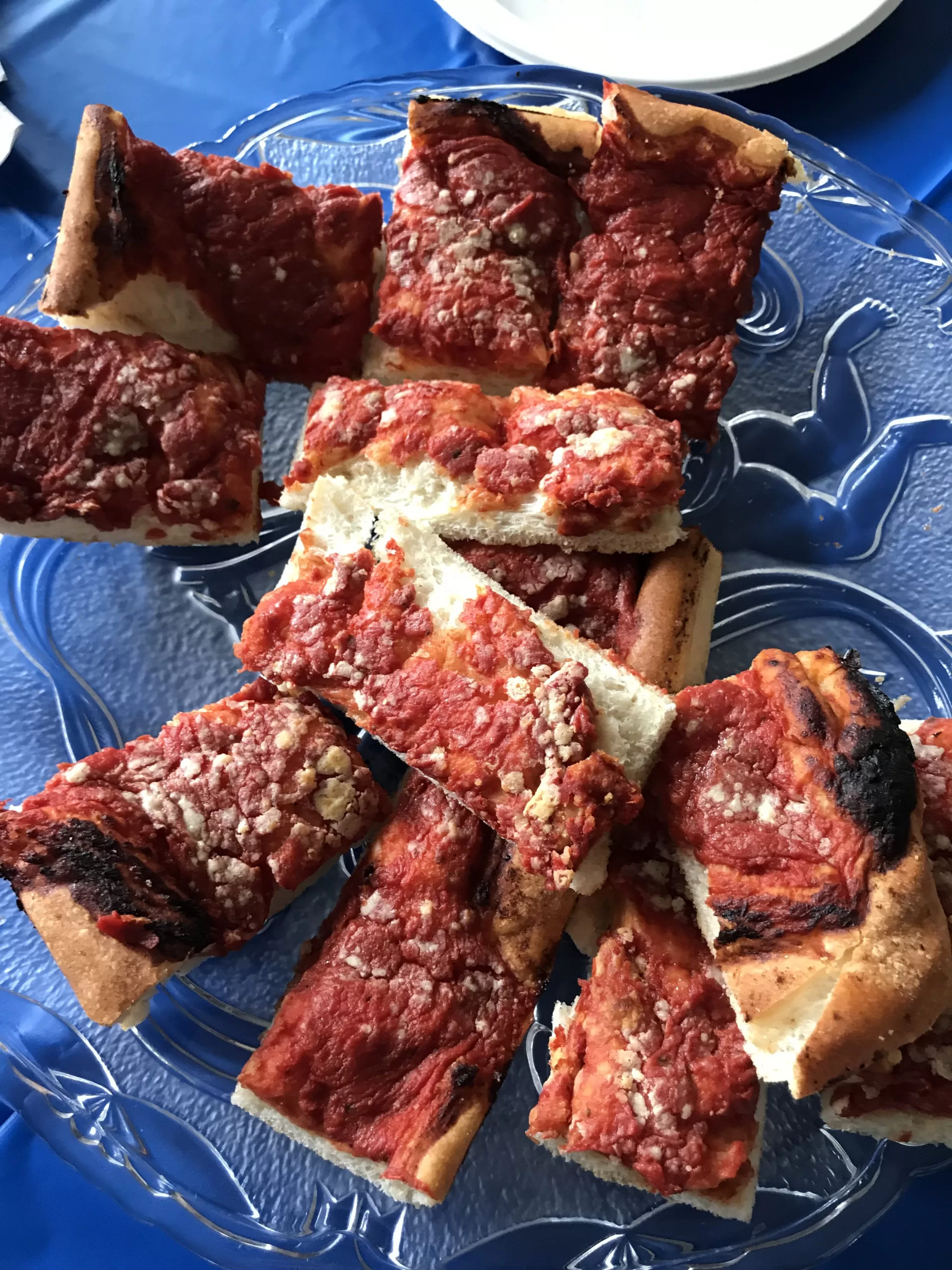 A table with a blue table cloth with a plate containing several pieces of Rhode Island-style bakery pizza.