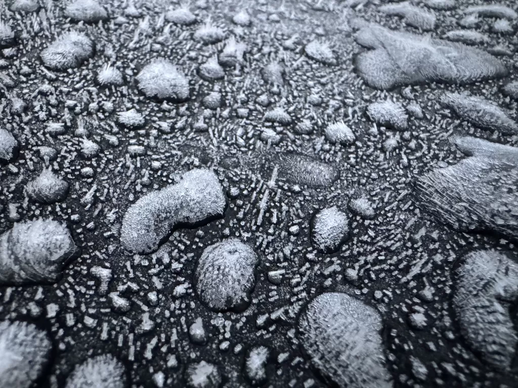 A close up of frozen water droplets and frost on the back of a black car.