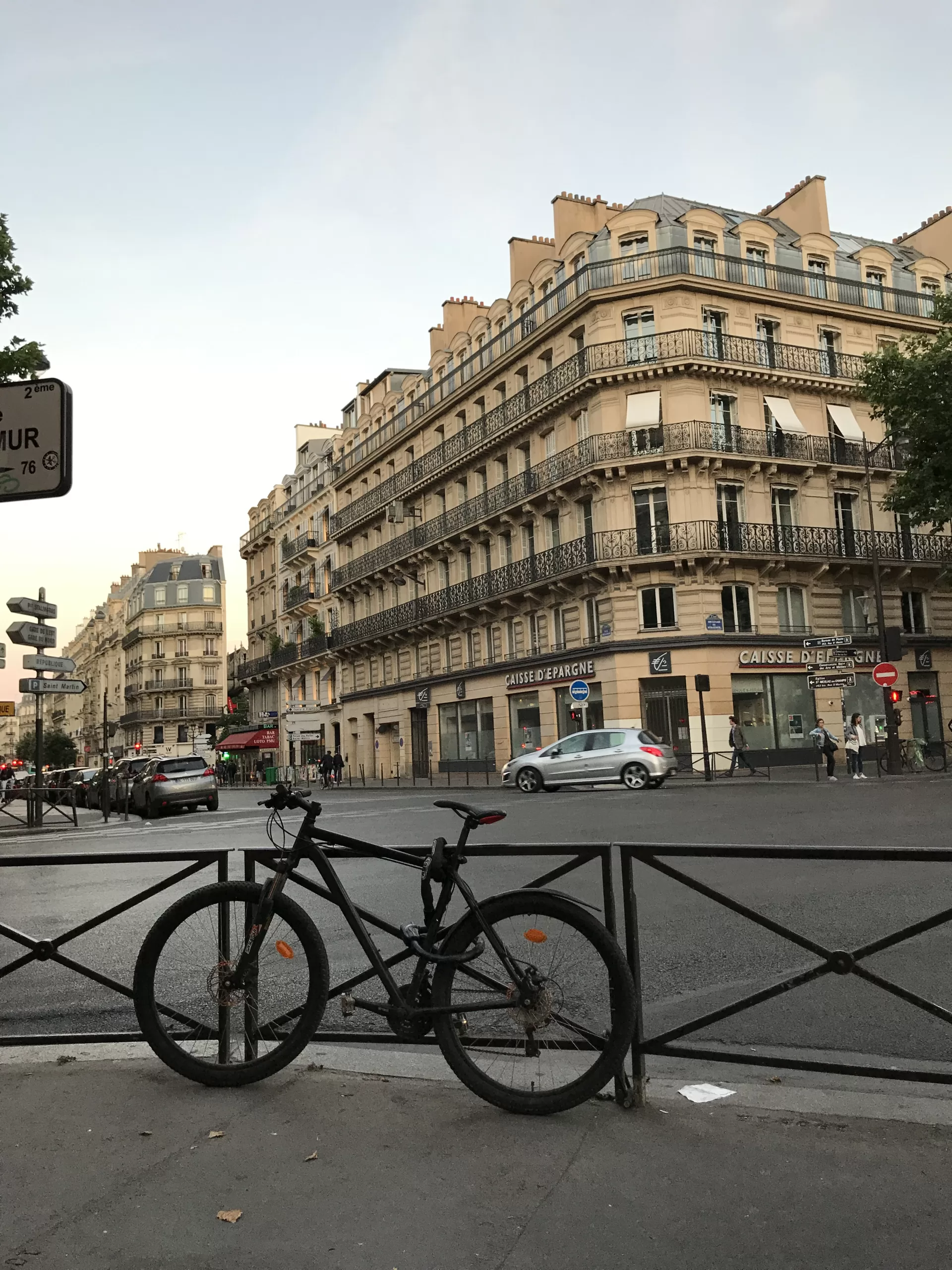 An intersection in Paris, France. There's a black railing along the edge of the sidewalk with a black bike chained to it.