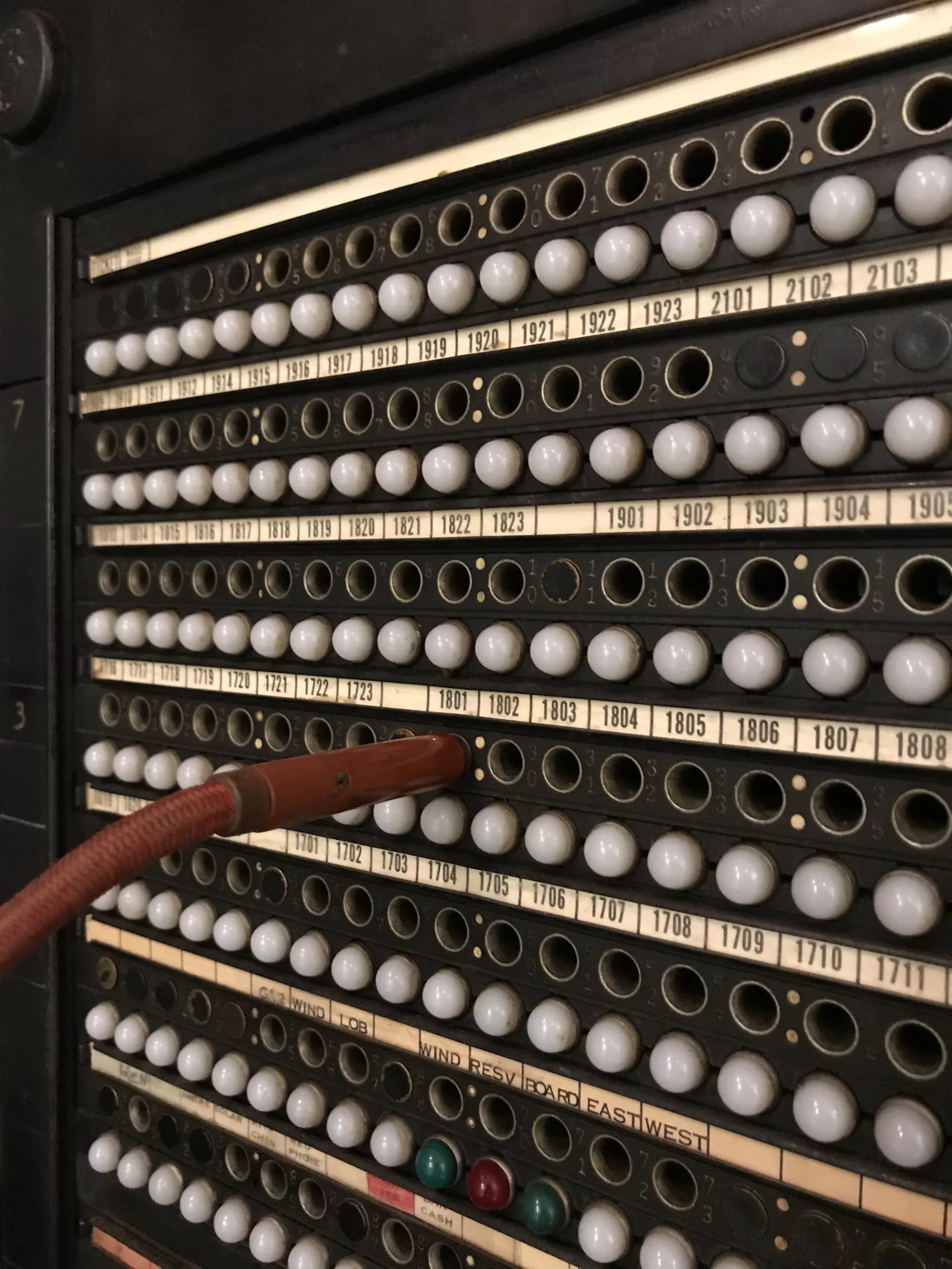 An old-style telephone switchboard which would have been used to connect to telephones on a circuit. A thick cord in the photo was used to connect the calls.