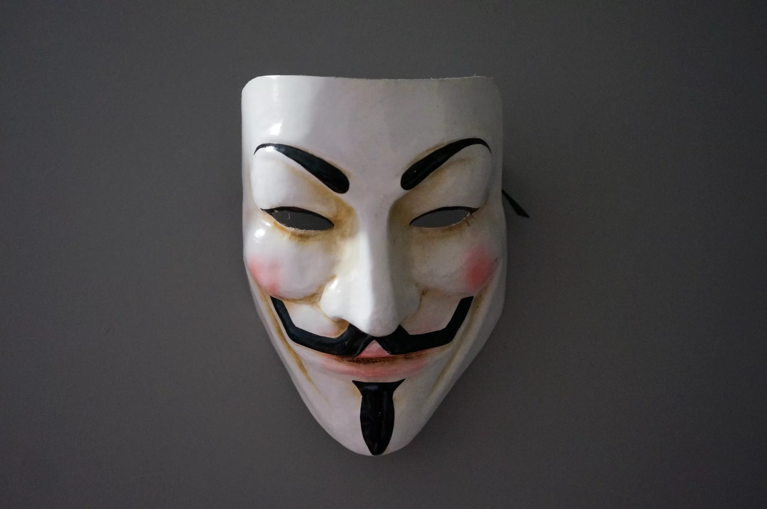 Guy Fawkes mask hanged in a grey wall.
