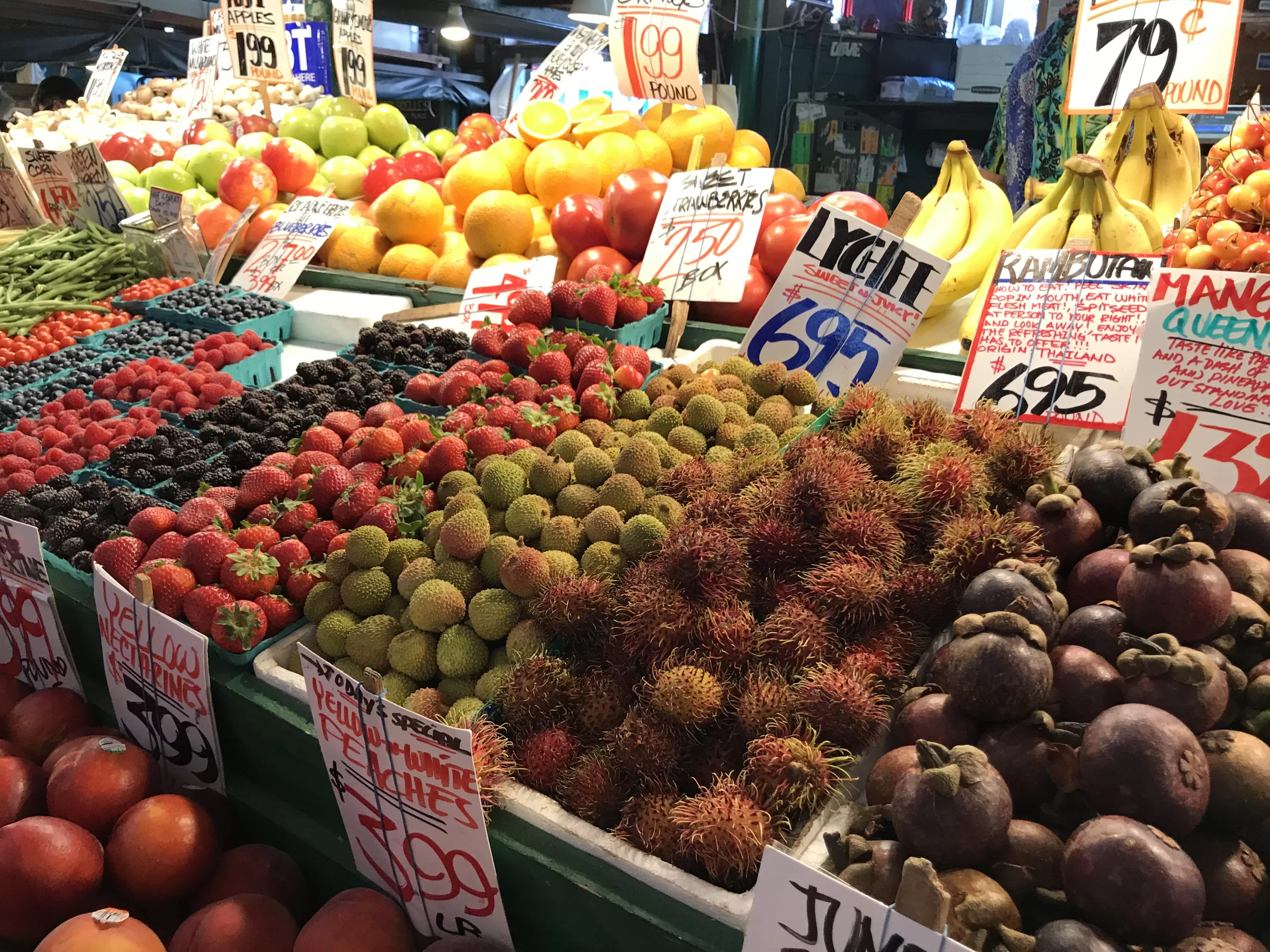 A colorful fruit stand inside Pike Place Market in Seattle, Washington featuring various berry and apple varieties, bananas, nectarines, and rambutan. =
