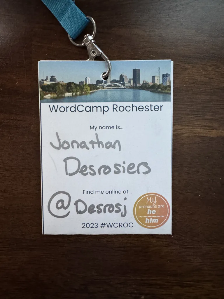 My WordCamp Rochester 2023 badge consisting of an event branded printed badge with my name and information written in with silver marker.