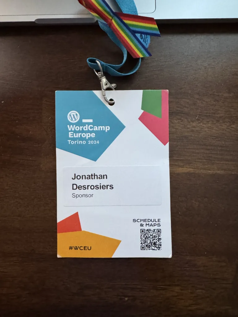 My WordCamp Europe 2024 Sponsor badge consisting of an event specific printed badge with a sticker label with my name and conference role.