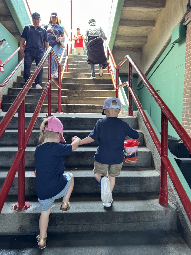 Two children going up concrete stairs to the bleachers at Fenway Park in Boston, Massachusetts.