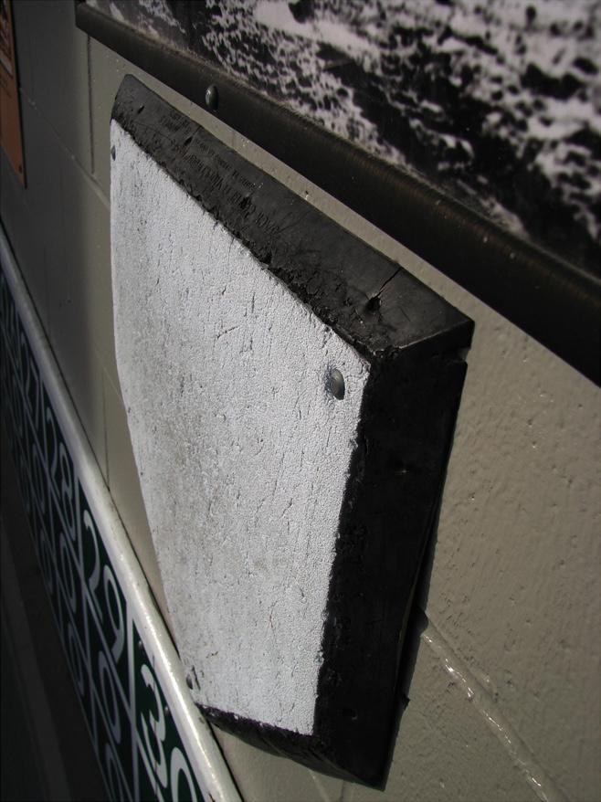 A home plate bolted to a white cinder block wall.