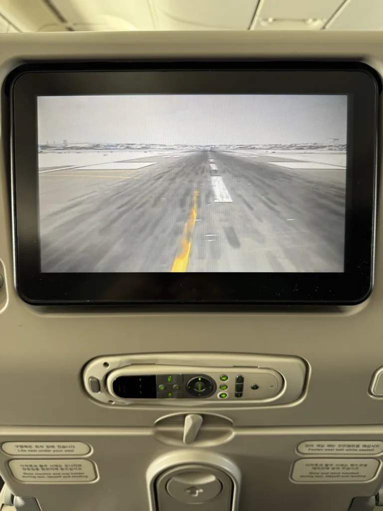 The seat back screen of an airplane seat showing the front facing camera on the aircraft. An empty snowy runway can be seen.
