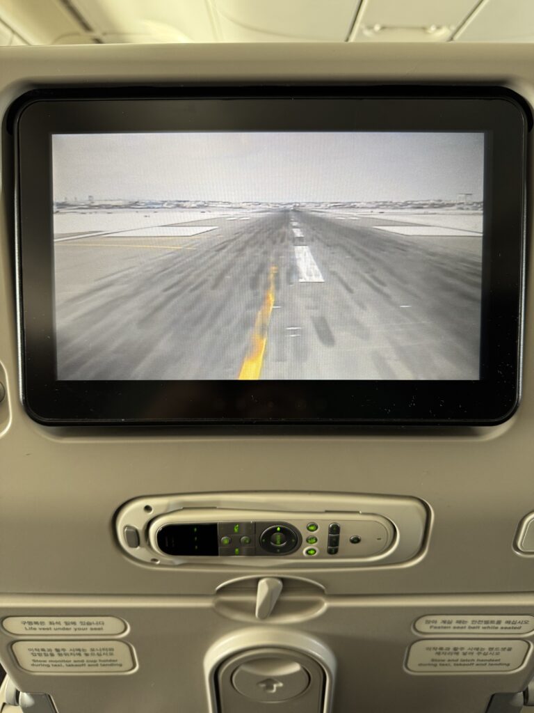 The seat back screen of an airplane seat showing the front facing camera on the aircraft. An empty snowy runway can be seen.