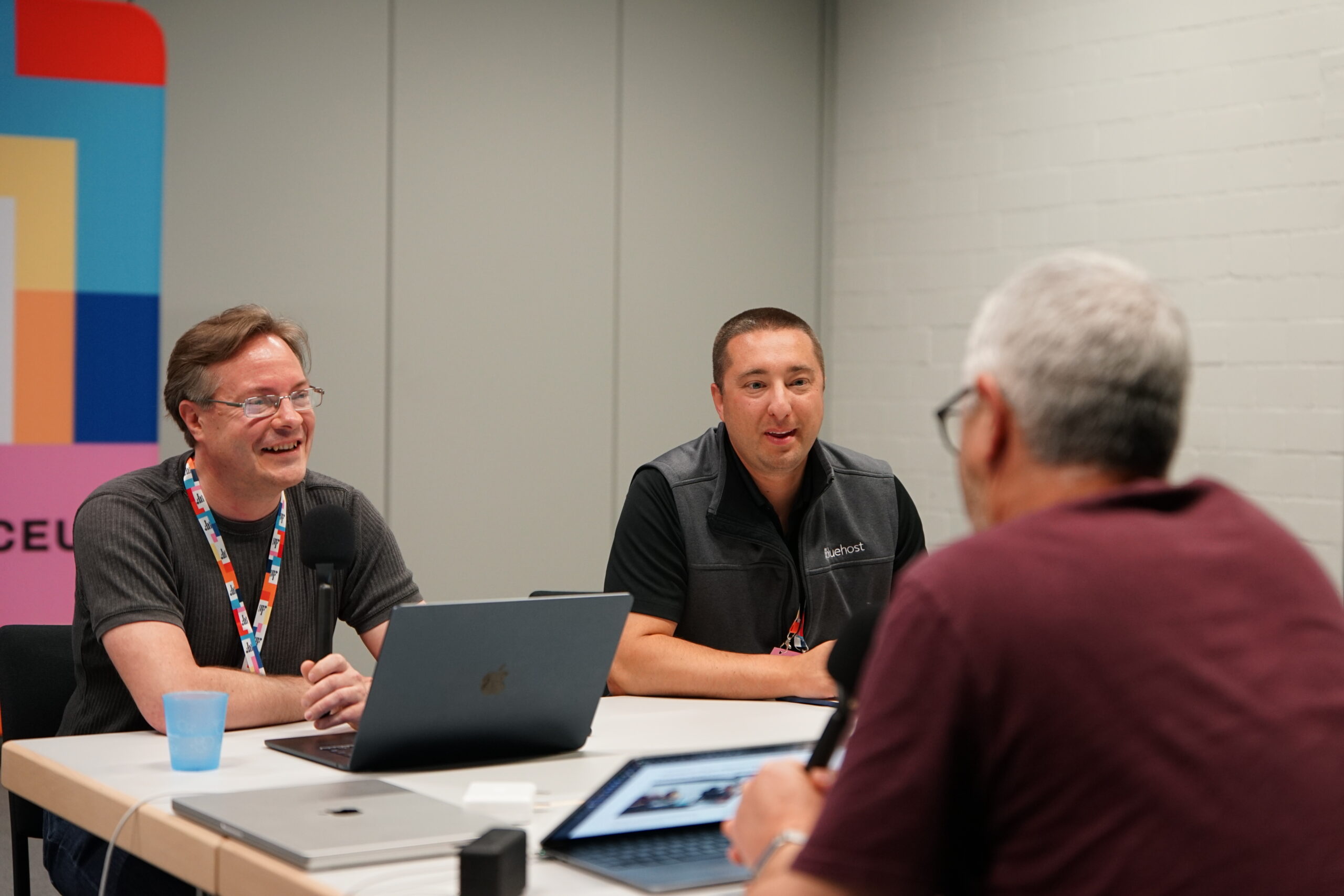 Jonathan Desrosiers and Joe Dolson laughing and talking to Nathan Wrigley while recording an episode of the WP Tavern Jukebox podcast. Nathan's back is to the camera and is out of focus in the foreground.