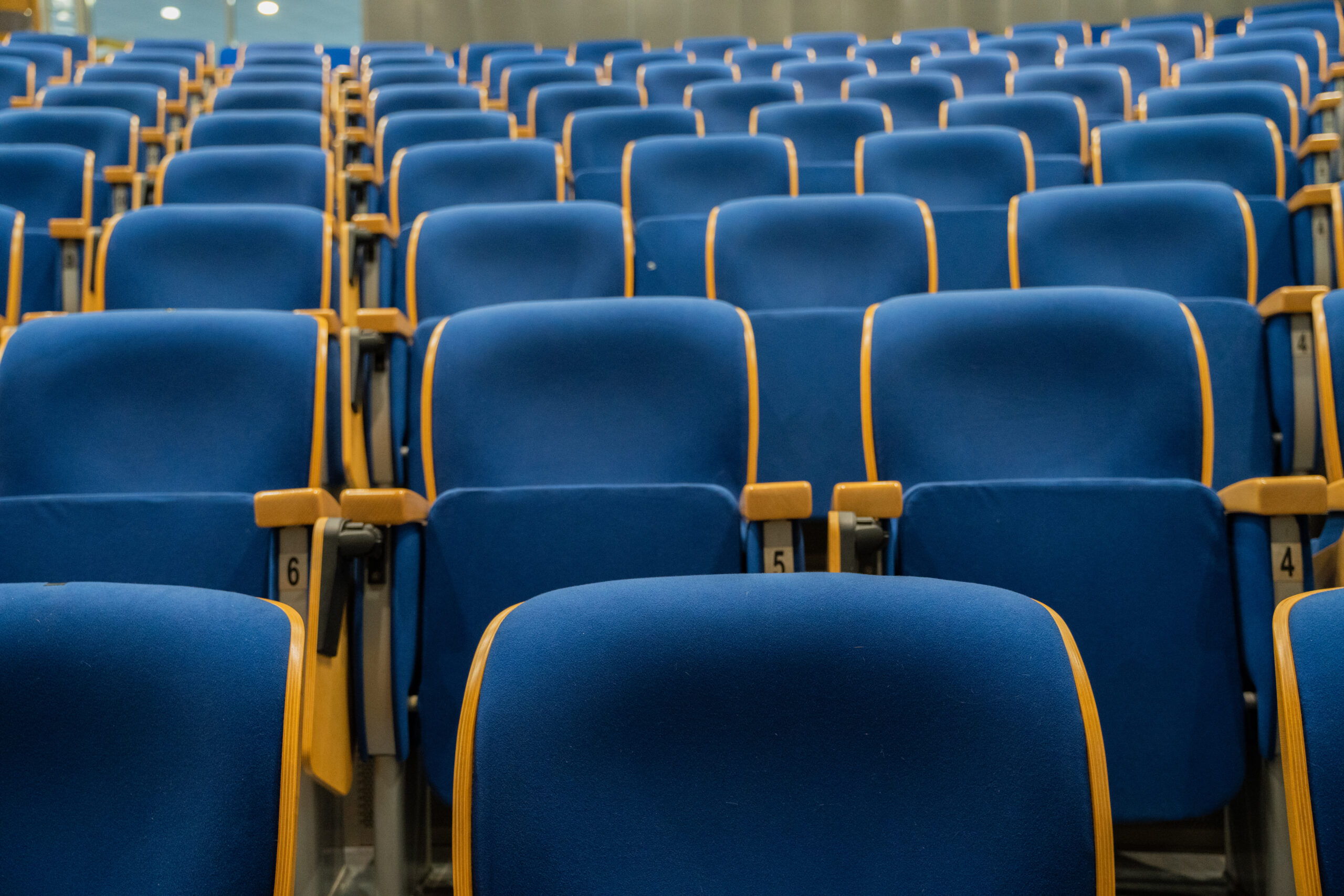 A large, empty auditorium with rows of numbered blue seats with yellow trim.