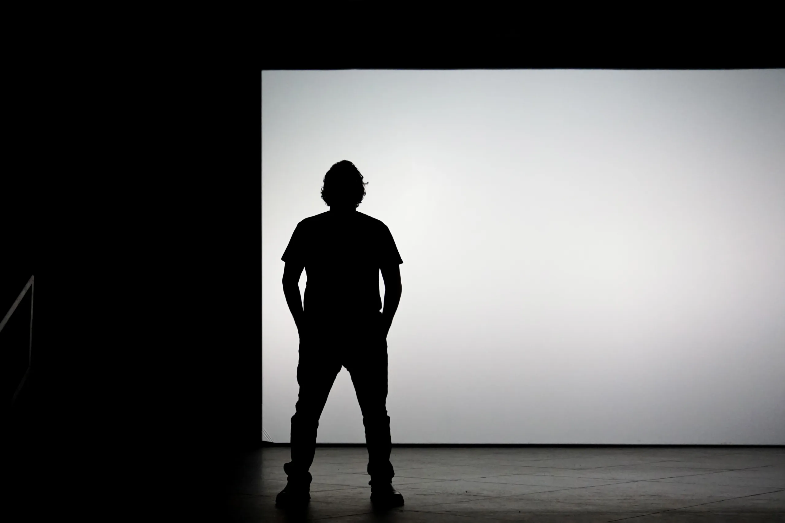 A person standing alone in front of a large, bright white screen, with only their silhouette visible against the light background.