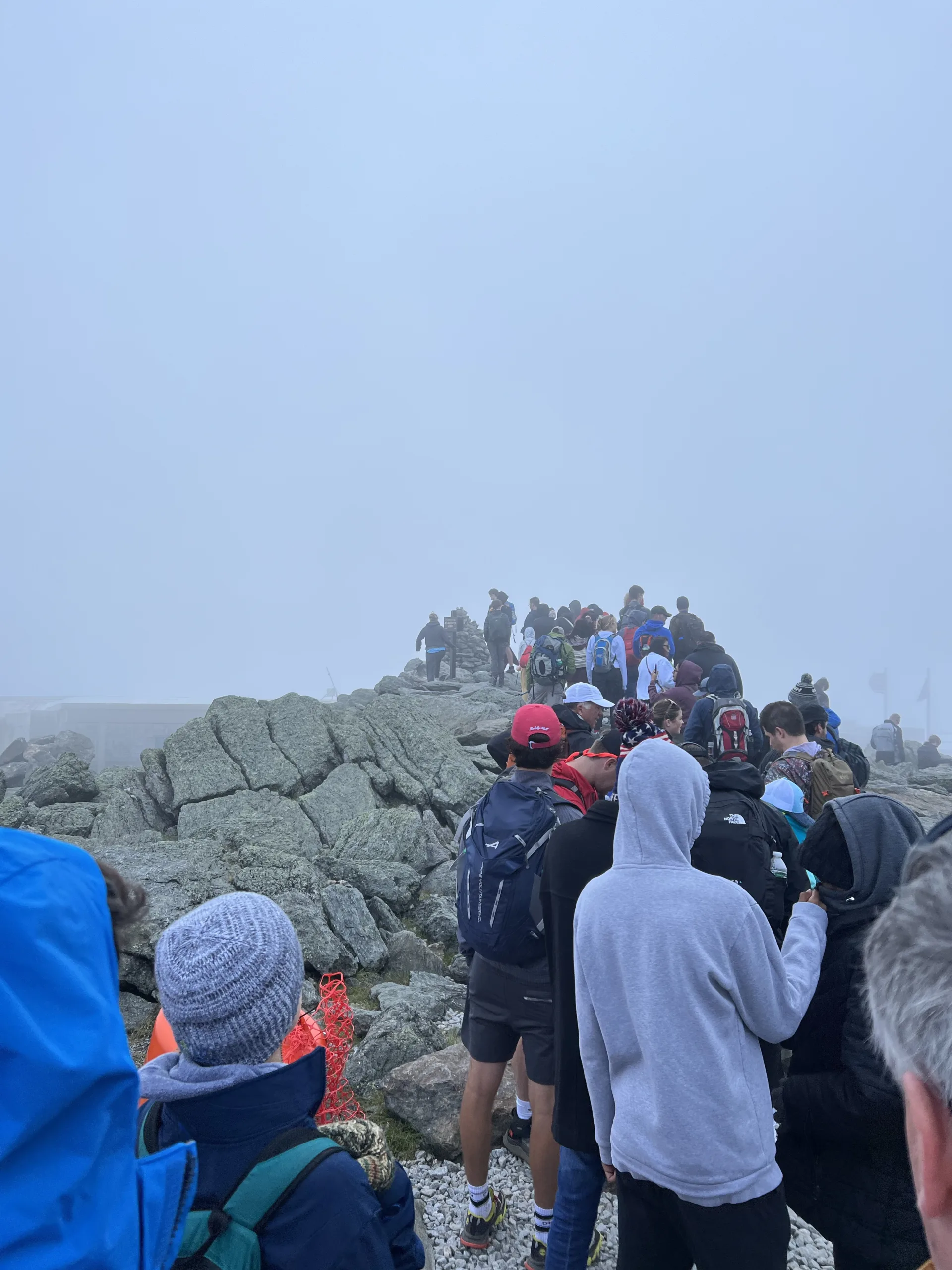 A long line of people at the top of Mount Washington lined up to take a photo with the summit sign.